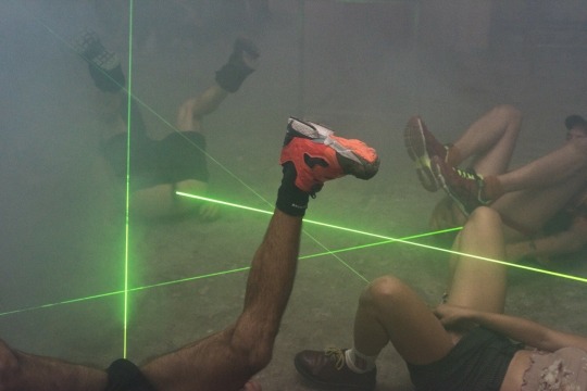 four men in a foggy area with green laser pointers pointing out their butts